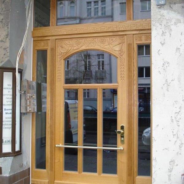 Kunstvoll geschnitzte Haustür nach Maß aus Eichenholz mit Glasfenstern und Messinggriffen an einem Gebäudeeingang.