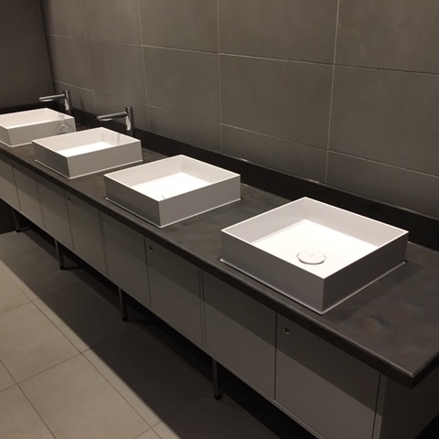 Maßgefertigte Badmöbel mit vier eckigen Aufsatzwaschbecken, dunkler Arbeitsplatte und weißen Unterschränken in einem modern gefliesten Badezimmer.