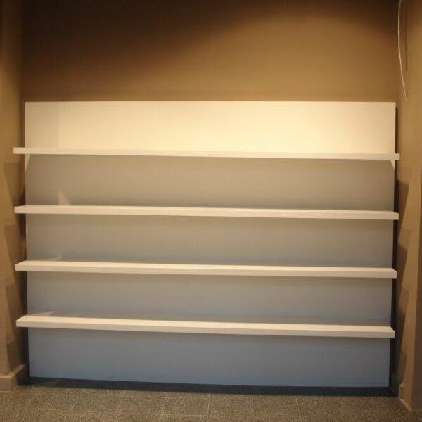 Weiße, maßgeschneiderte Ladenbau-Regale in einem leeren Raum mit einer Ecke links und grauem Bodenbelag.