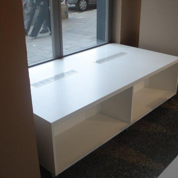 Modernes, weißes Ladenregal auf Rollen, maßgefertigt, an einem Schaufenster, durch das Passanten und städtisches Leben zu sehen sind.