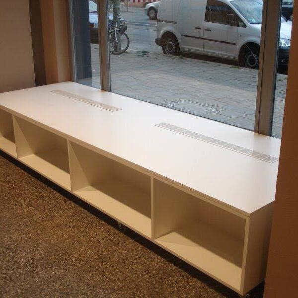 Ein weißes, maßgeschneidertes Ladenregal steht vor einem Schaufenster mit Blick auf die Straße.