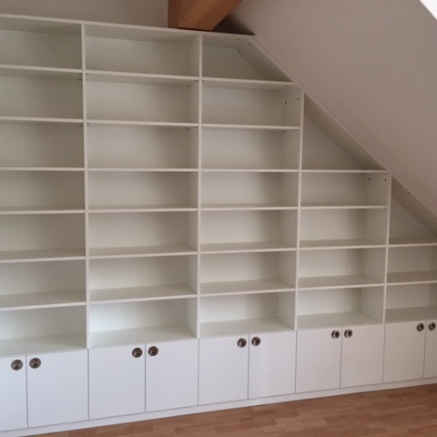 Großes, weißes Regal nach Maß, das sich einer Dachschräge anpasst, mit Schrankfächern im unteren Bereich.