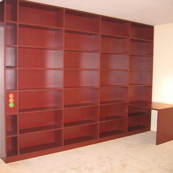 Ein großes, wandfüllendes Regal nach Maß in dunklem Holz, neben einem Schreibtisch in einem hellen Raum.