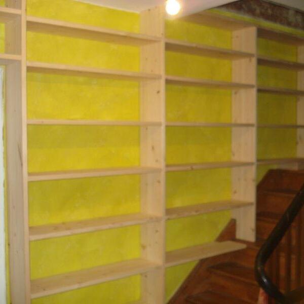 Unvollendetes Regal nach Maß vor gelber Isolierung an einer Treppenhauswand im Bauzustand.