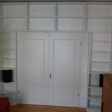 Maßgefertigte weiße Regalwand mit vielen Fächern, die perfekt über und neben eine Doppeltür passen.