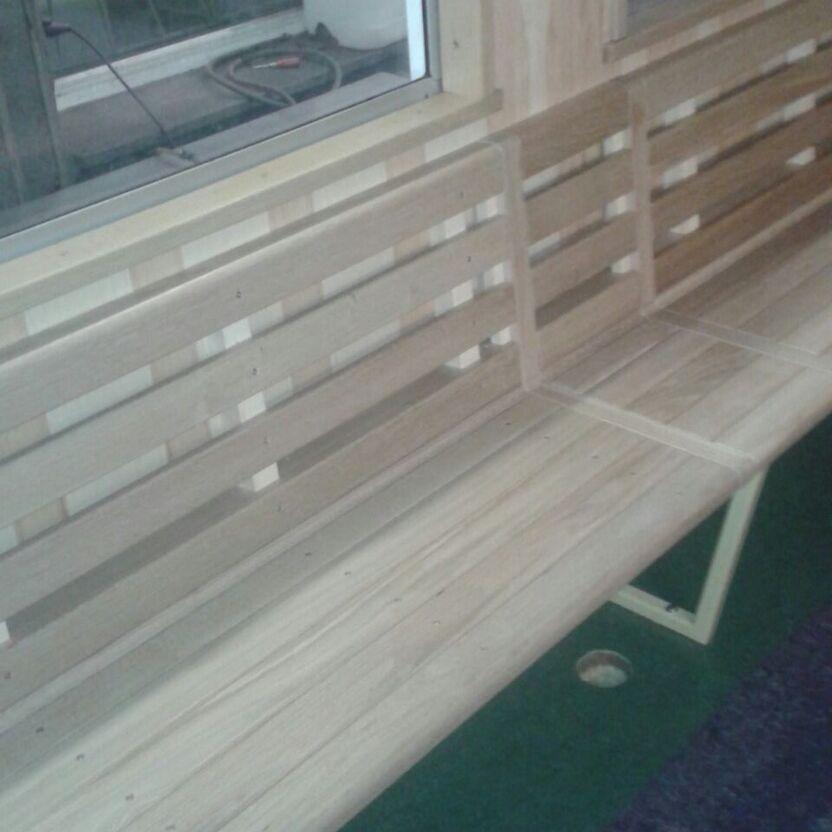 Maßgefertigte Holzsitzbank für den Wagonausbau nach Maß, auf grünem Teppich, neben einem Fenster mit Blick nach draußen.