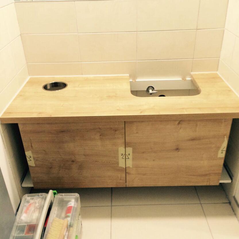 Moderner Waschtisch mit Holzdekor-Oberfläche und Unterschrank in einem gefliesten Badezimmer, teilweise in der Montage.