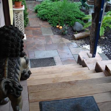 Treppenabgang aus Holz neben großer Löwenfigur vor Hauseingang