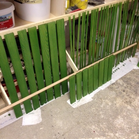 Grüne Holzlamellen von Fensterladen nach Maß zum Trocknen aufgestellt in einer Werkstatt.