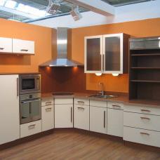 Eck-Küche nach Maß mit beige-farbenen Schränken, dunklen Arbeitsplatten und eingebauten Elektrogeräten.