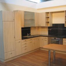 Maßgefertigte Küchenzeile mit hellen Holzfronten, schwarzer Arbeitsfläche und integriertem Esstisch.