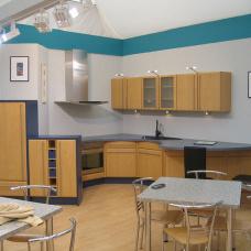 Funktionale Küche nach Maß mit Holzschränken, schwarzem Arbeitsbereich und einer Essecke, kontrastiert durch blaue Wände.