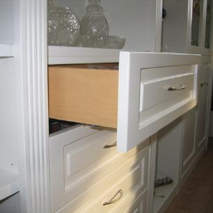 Maßgefertigter weißer Schrank mit edlen Griffen und einer geöffneten Schublade, die den hochwertigen Holzinnenraum zeigt.