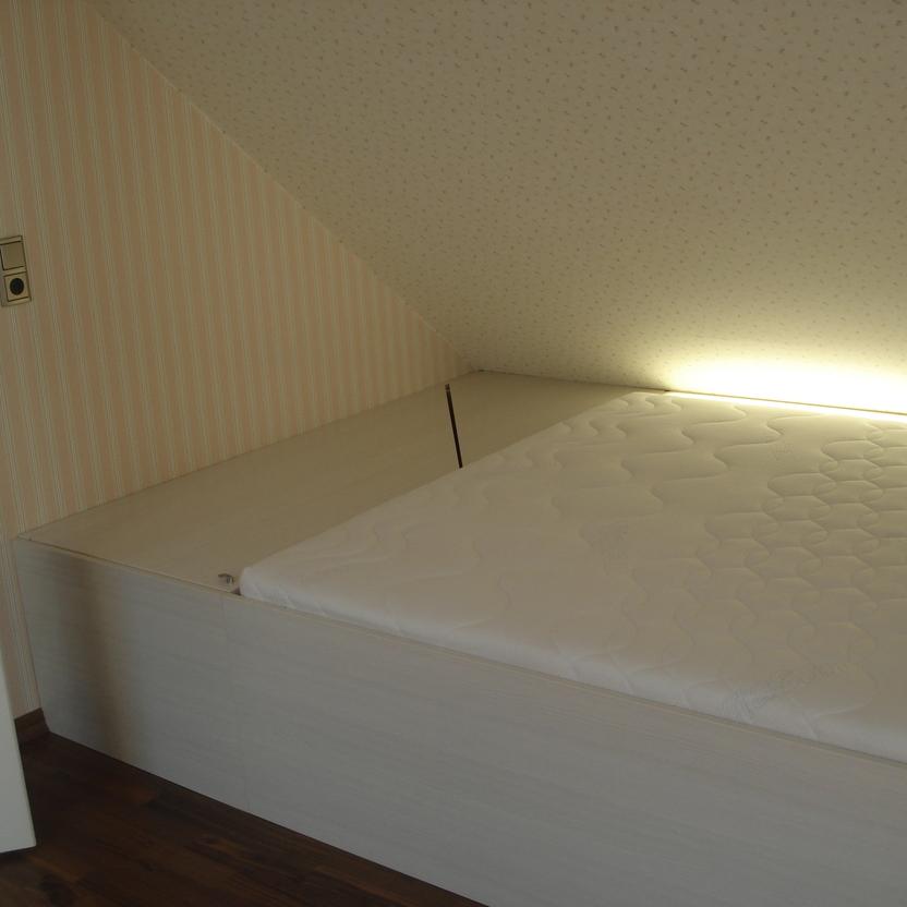 Maßgefertigtes Bett mit integrierter Beleuchtung und Stauraum, perfekt in eine Nische unter einer Dachschräge eingepasst.