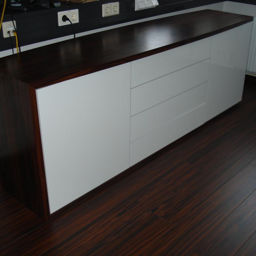 Modernes Sideboard in Hochglanzweiß mit dunkler Holzablage, ein Beispiel für maßgefertigte Büromöbel.
