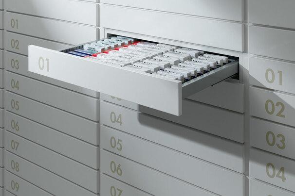 Detailaufnahme von schmalen weißen Medikamentenschubläden mit dezenter Nummerierung und sichtbarer Medikamentenaufteilungen.