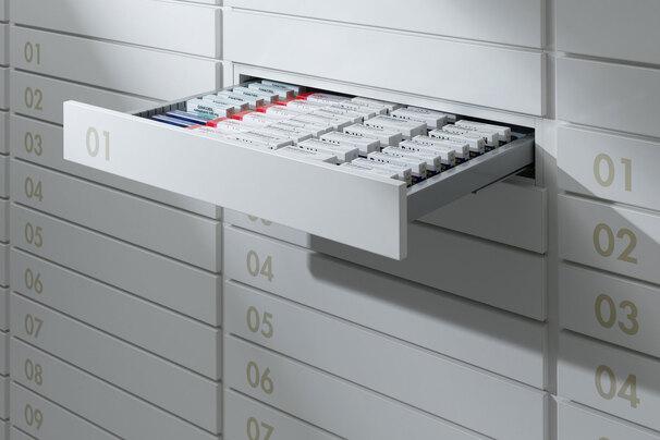Detailaufnahme von schmalen weißen Medikamentenschubläden mit dezenter Nummerierung und sichtbarer Medikamentenaufteilungen.